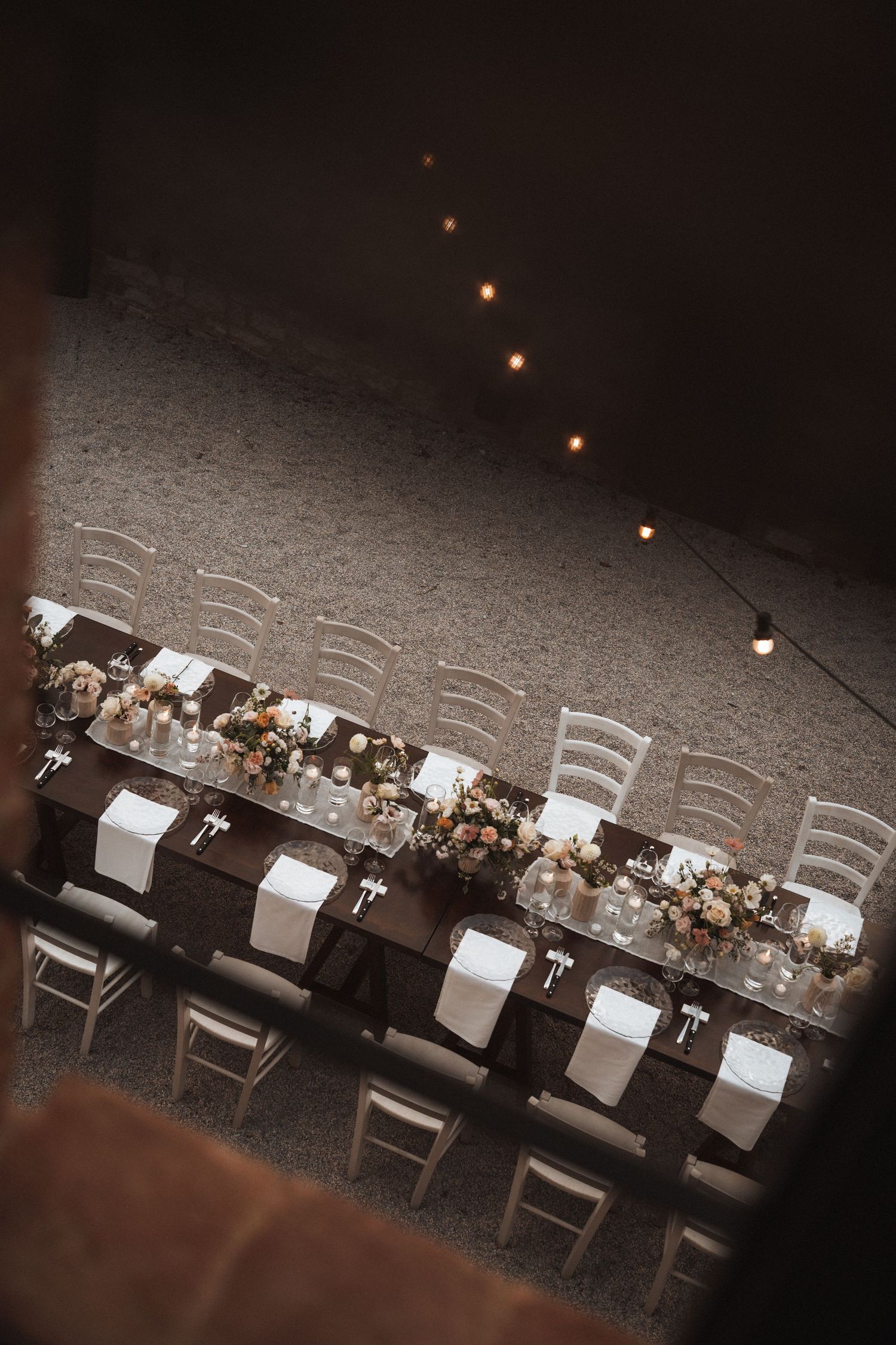 Overhead view of a formal wedding reception table with string lights and place settings.