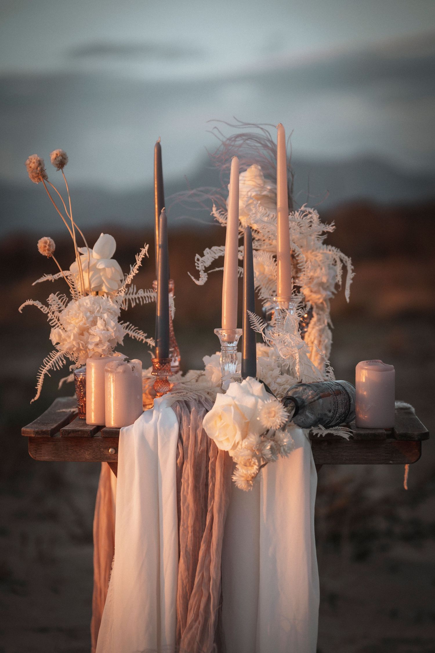 Ethereal wedding table decor with tall candles, dried flowers and flowing fabrics in moody sunset lighting.
