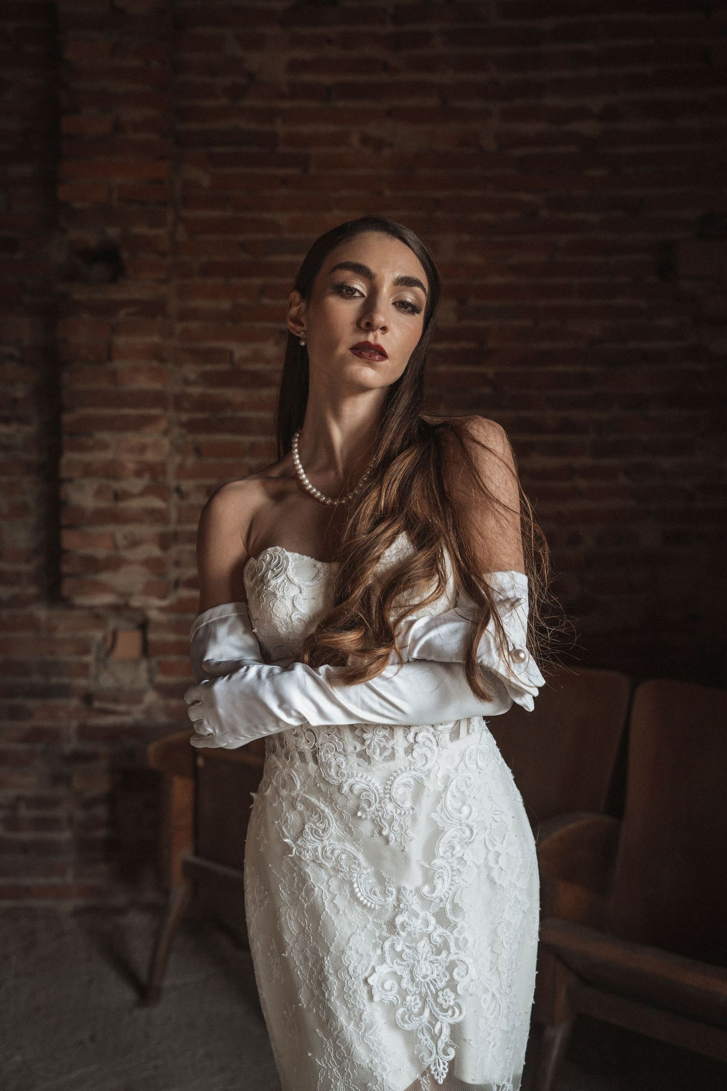 Elegant bridal portrait showcasing off-shoulder white lace gown against rustic brick backdrop.