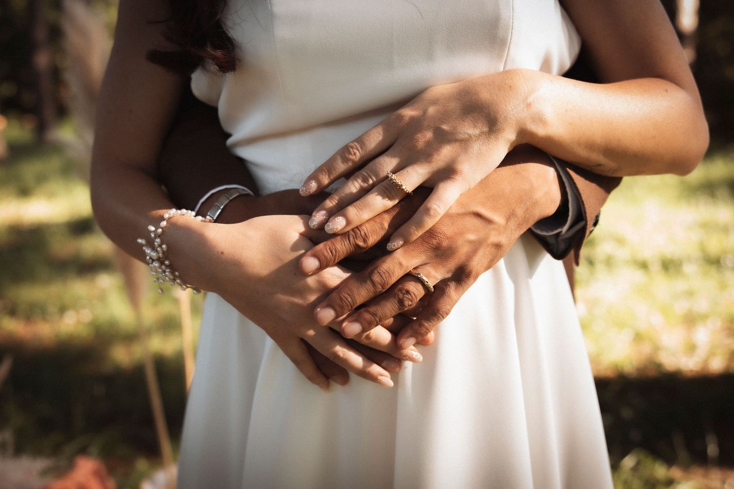 Close-up detail of hands resting gently on a white dress fabric in warm natural lighting.