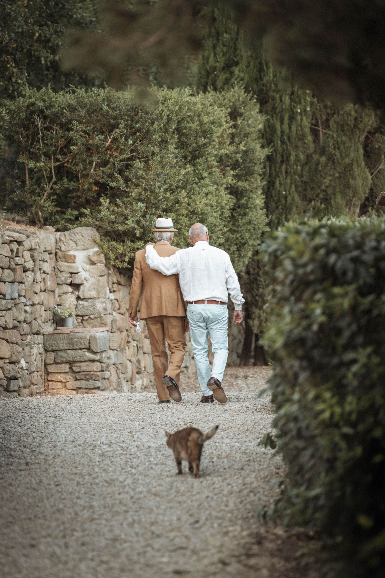 Elderly couple walking together along a stone wall path in a garden.