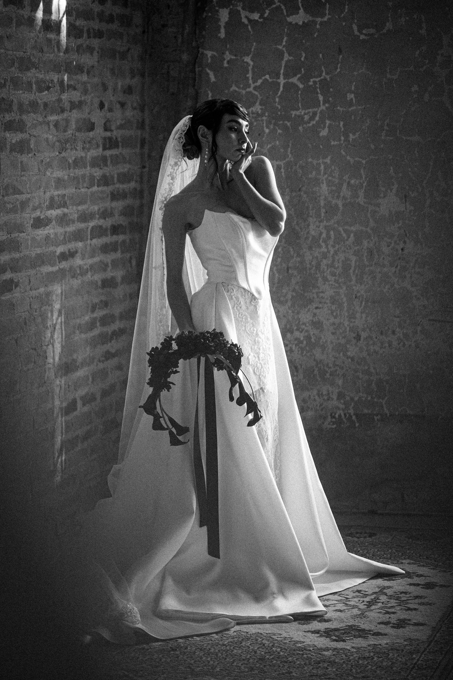 Black and white photograph of flowing white dress against textured brick wall.