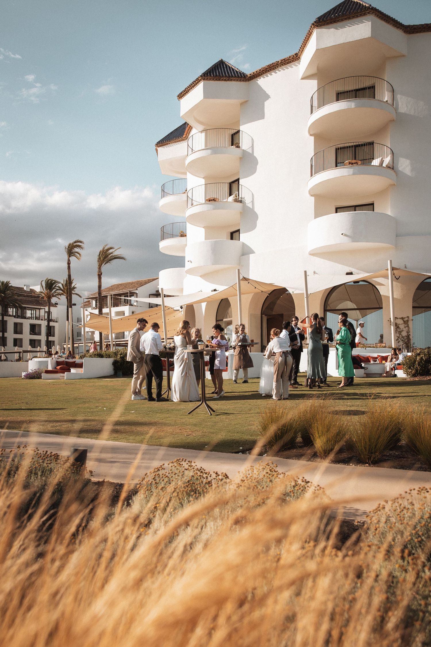 Modern white Mediterranean-style venue with palm trees and ocean views hosts an outdoor wedding ceremony.