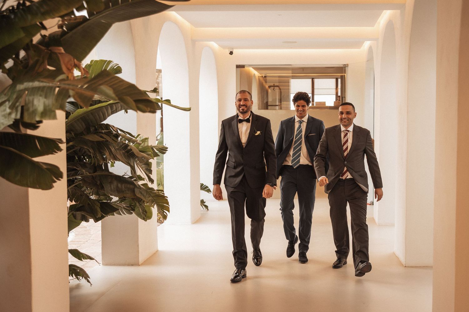 Group walking through elegant white hallway decorated with large potted plants.