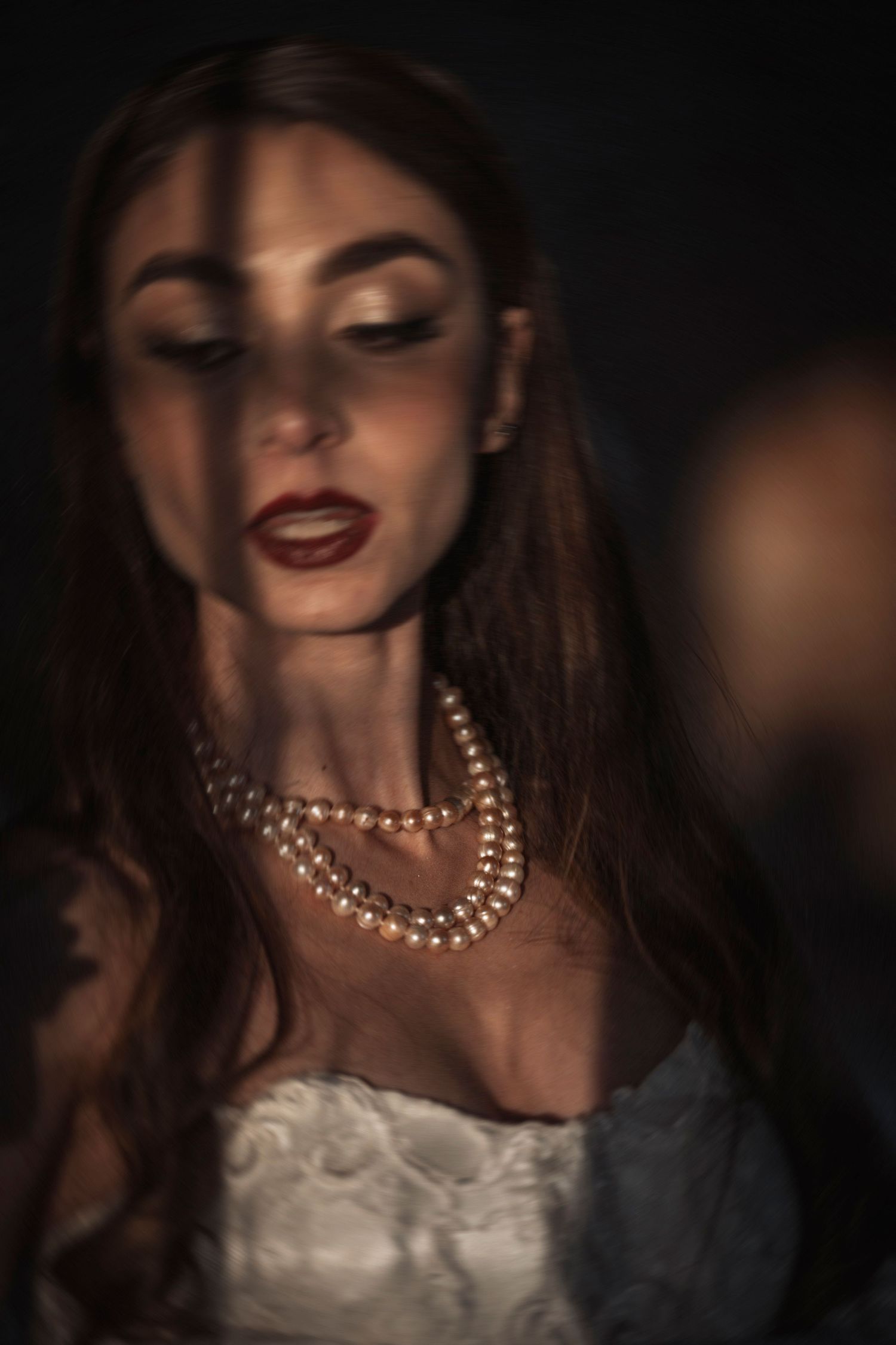 Pearl necklace and lace details illuminated by dramatic lighting.