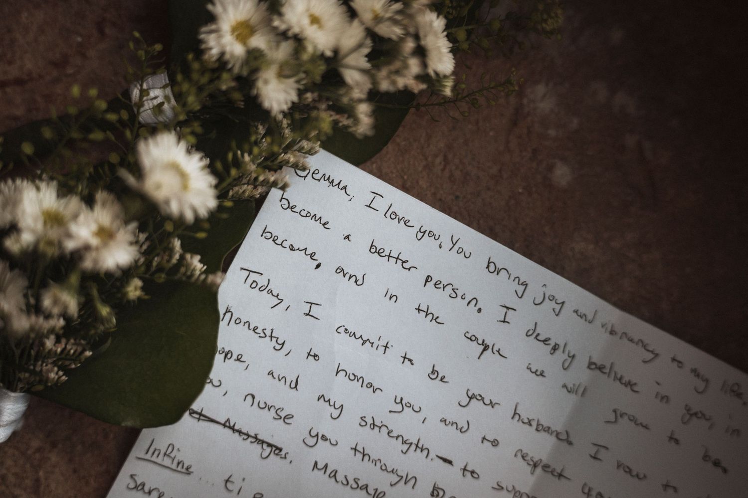 Handwritten wedding vows and white flowers on a rustic wooden surface.