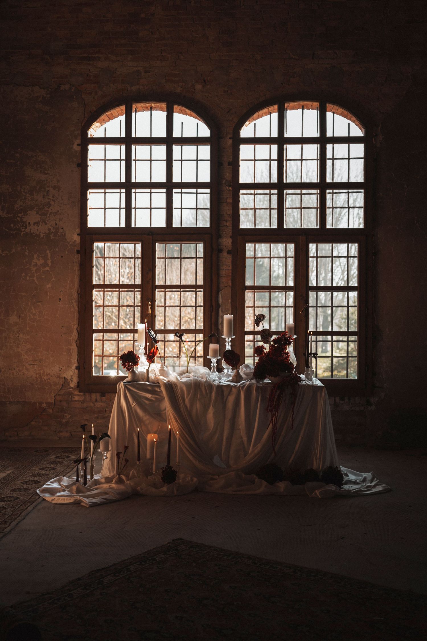 Dramatic window lighting illuminates an elegant table setting in a rustic brick interior space.