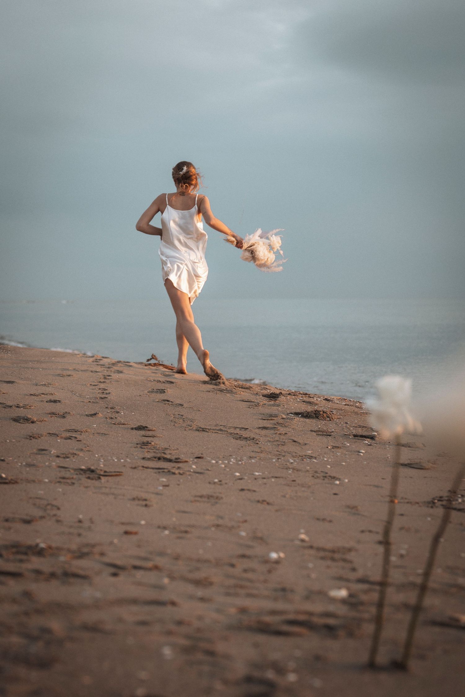 A figure in white walks along a misty beach shoreline at dusk.