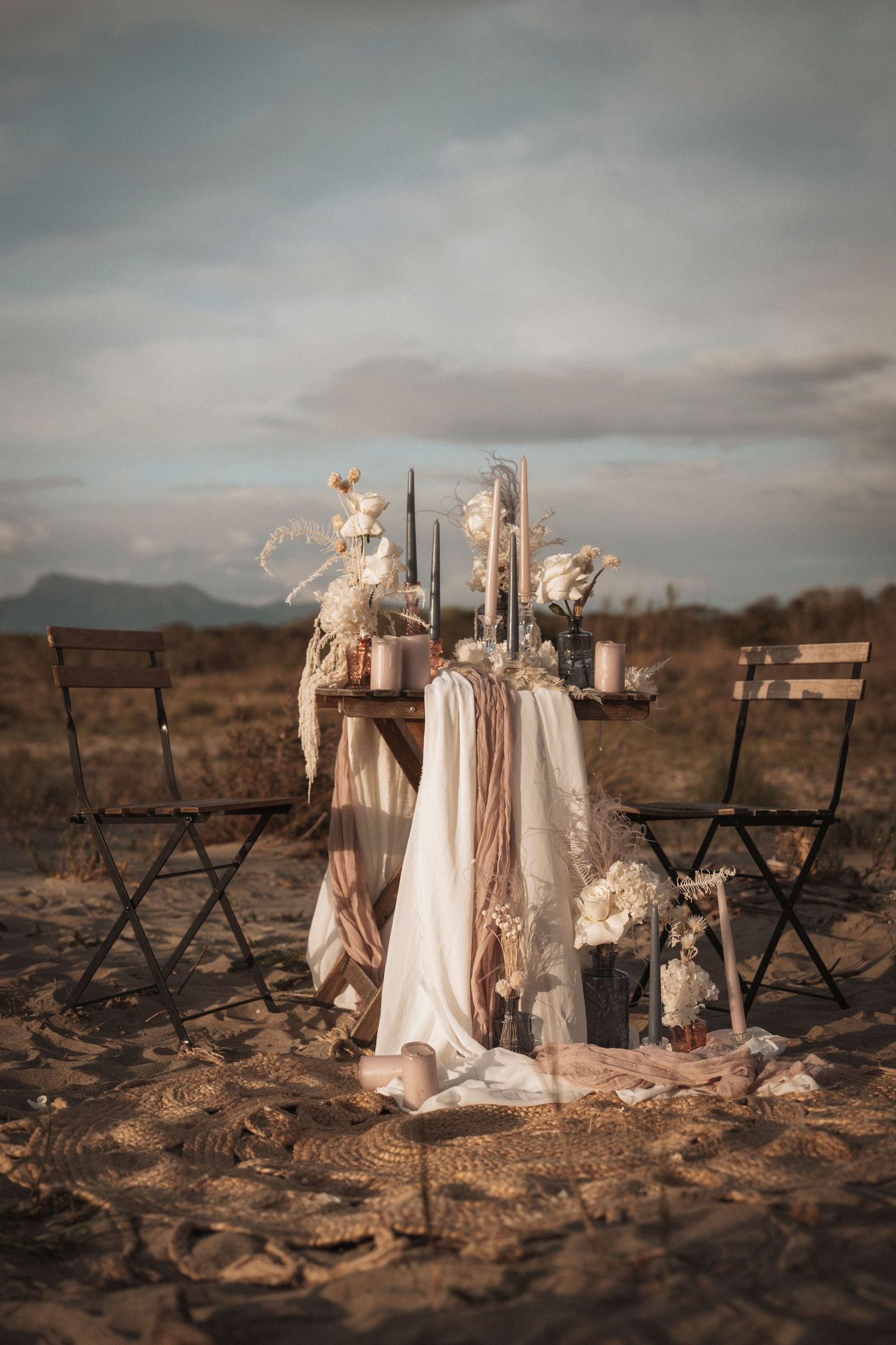 Rustic wedding decor with vintage chairs, floral arrangements and draped fabric in a desert setting.