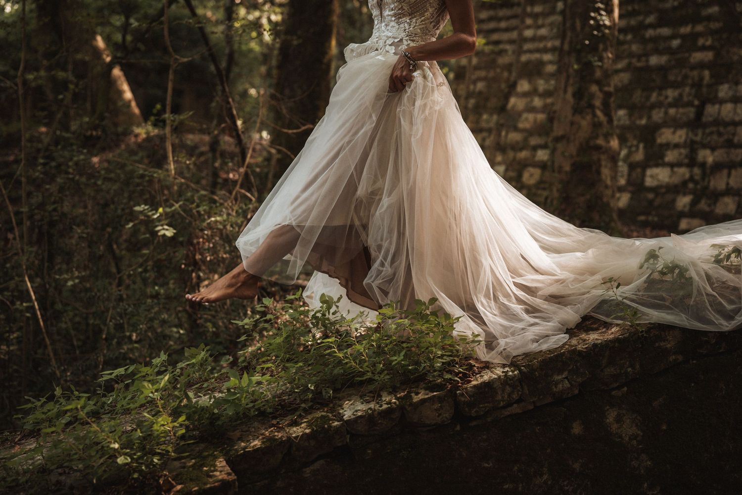 Flowing wedding dress train creates dreamy effect in forest setting.