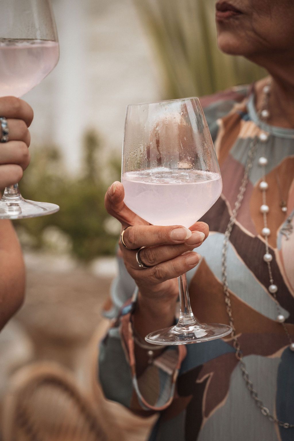 Close-up of hands holding rose wine glasses at an elegant outdoor event.