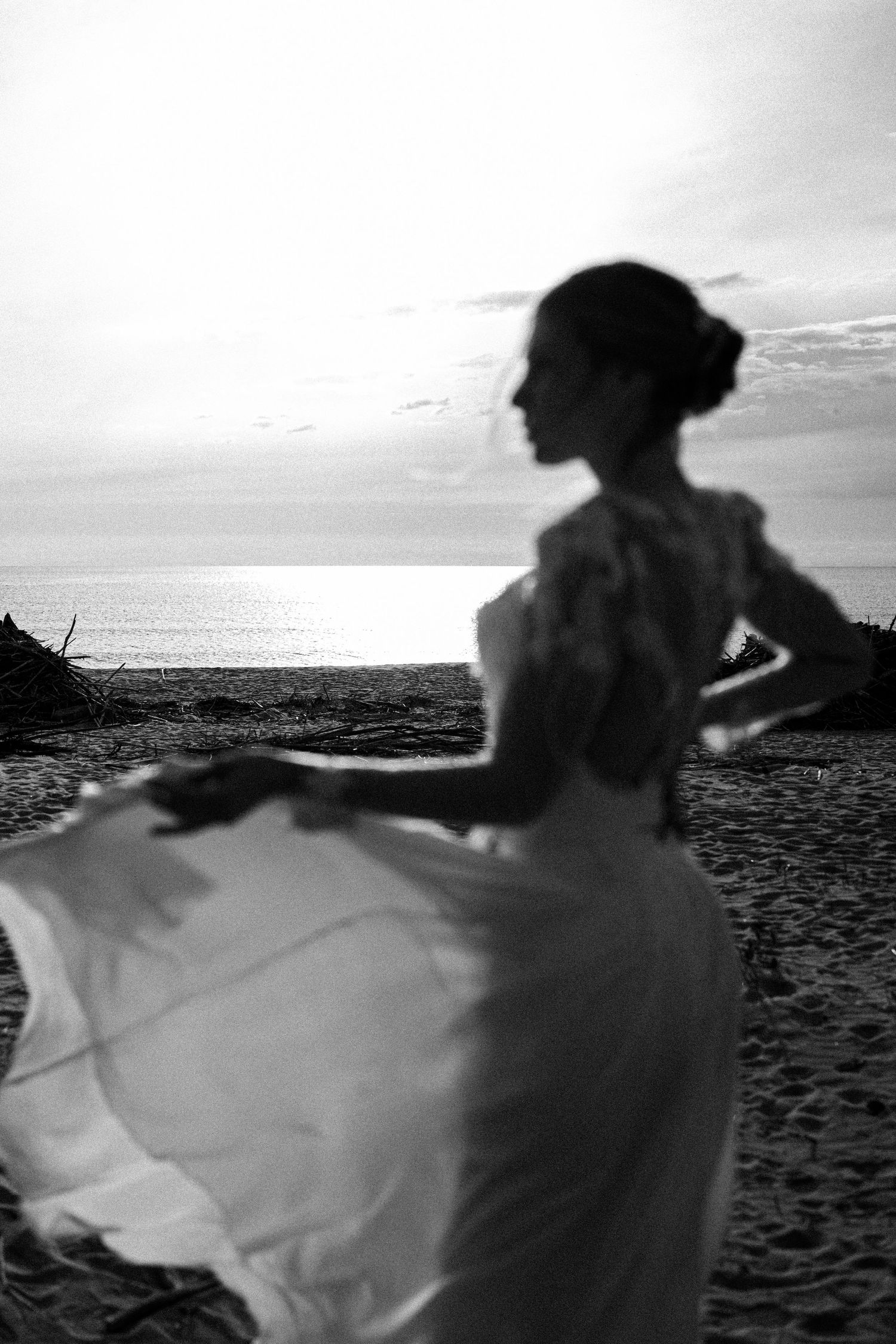Silhouetted figure on a beach with flowing fabric creating a dramatic motion effect against a bright sky.