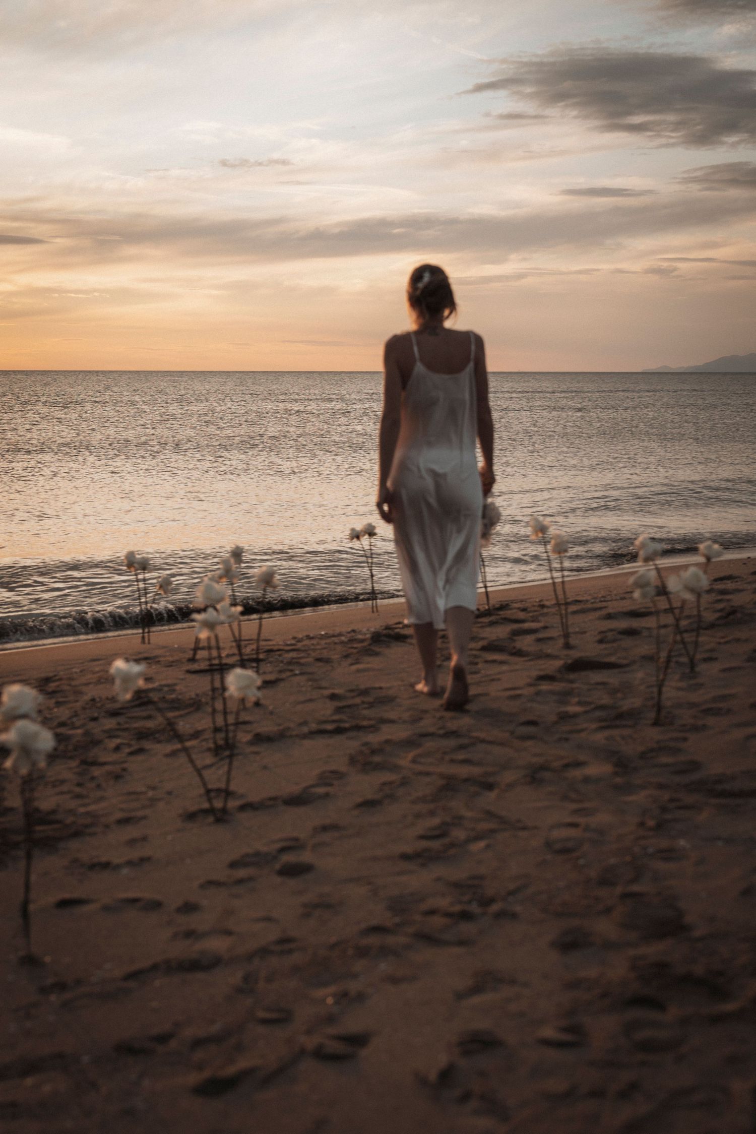 Silhouette of a white dress against a golden sunset on a beach lined with glowing candles.