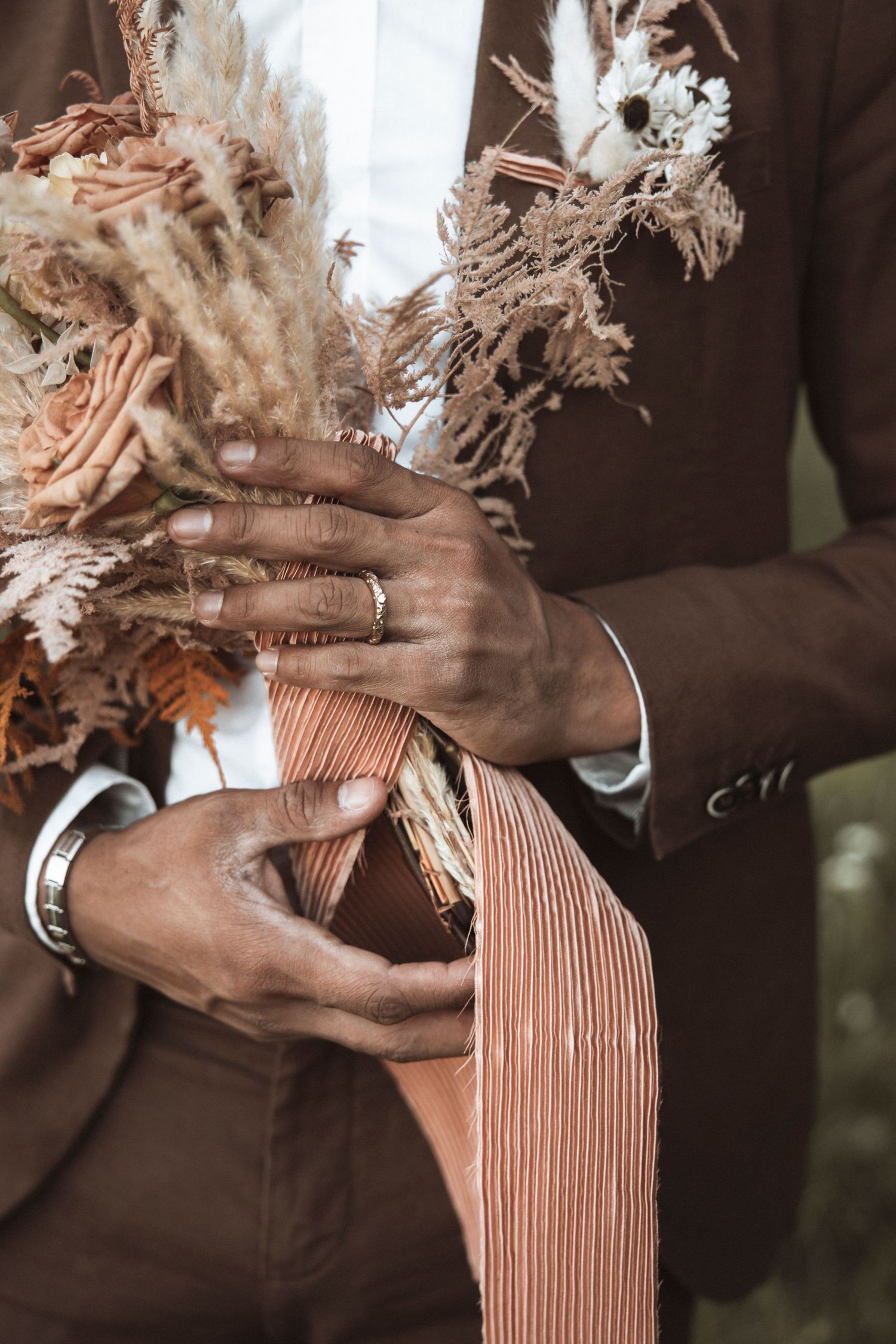 Close-up of hands holding dried flowers and fabric with elegant jewelry details.