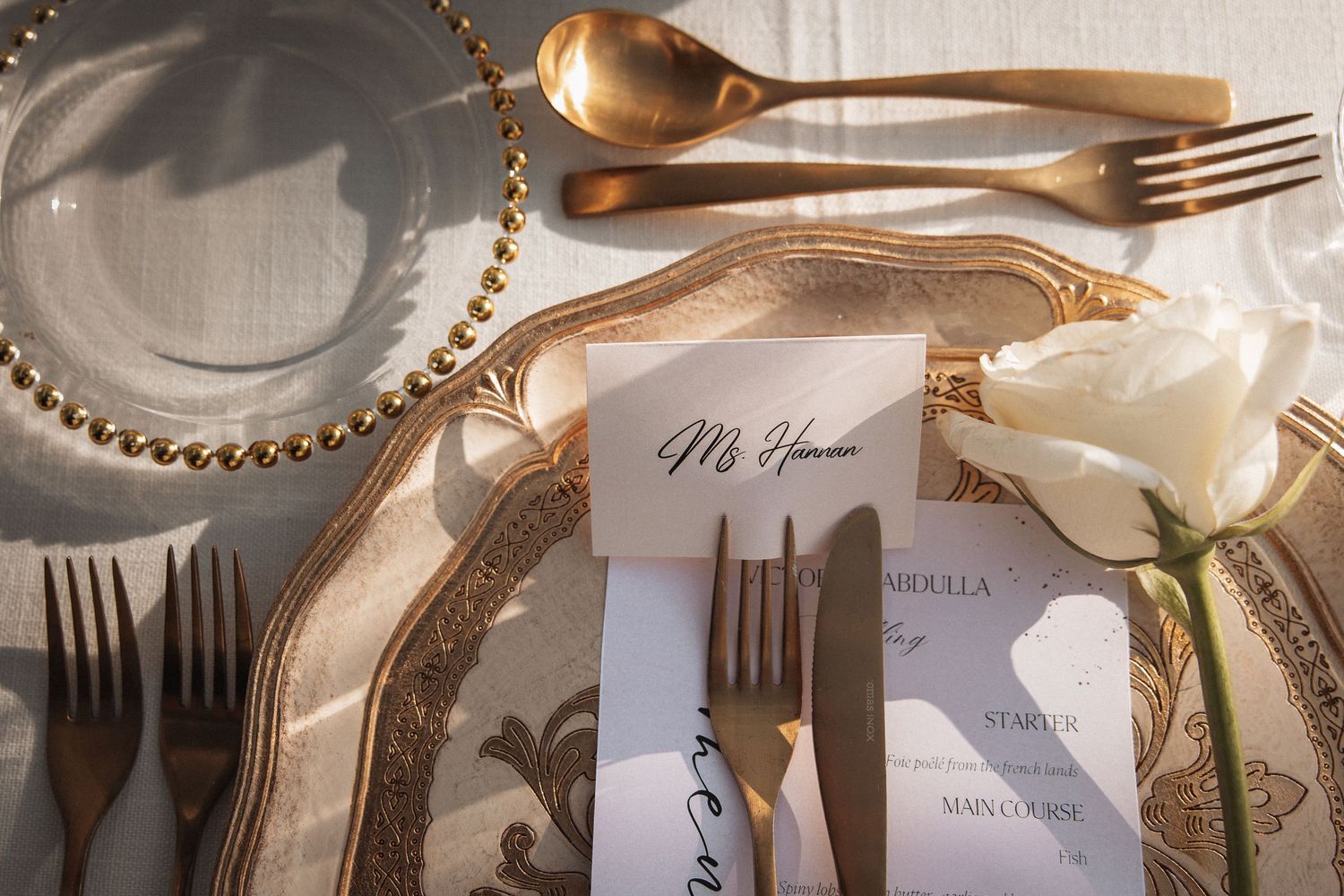 Close-up of elegant gold place settings and name cards at a formal wedding reception.