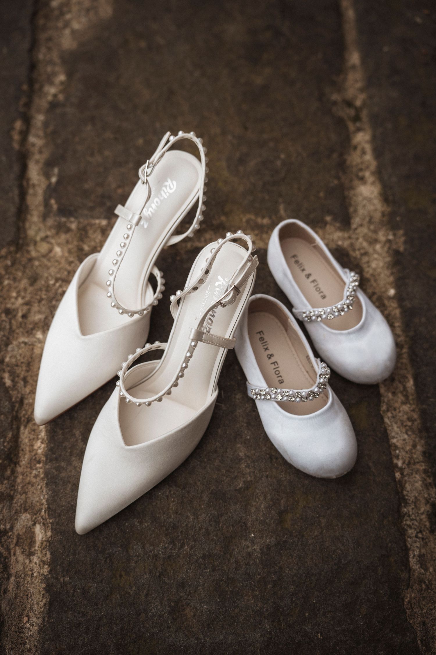 Elegant white bridal shoes with pearl embellishments arranged on a rustic wooden surface.