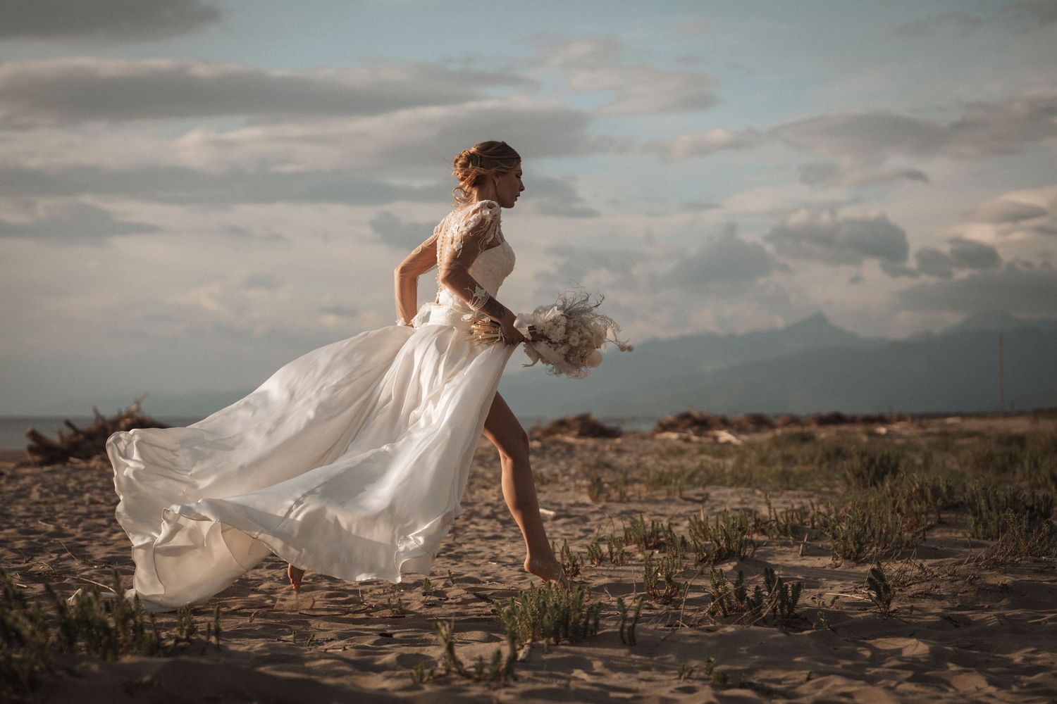 A flowing white wedding dress catches the golden light at sunset in a desert landscape.