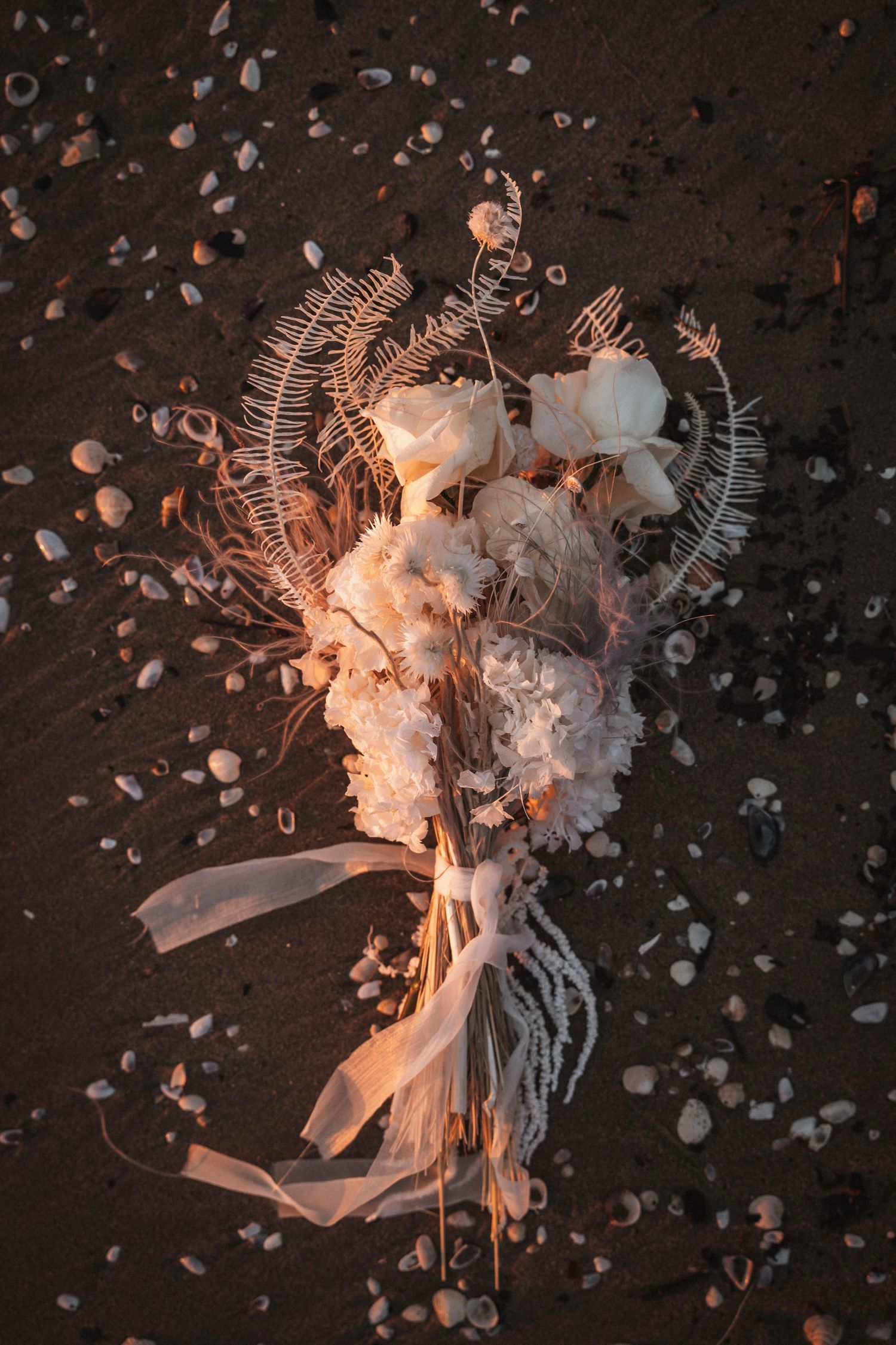 Ethereal white floral arrangement with ribbons scattered on dark surface amid scattered light reflections.