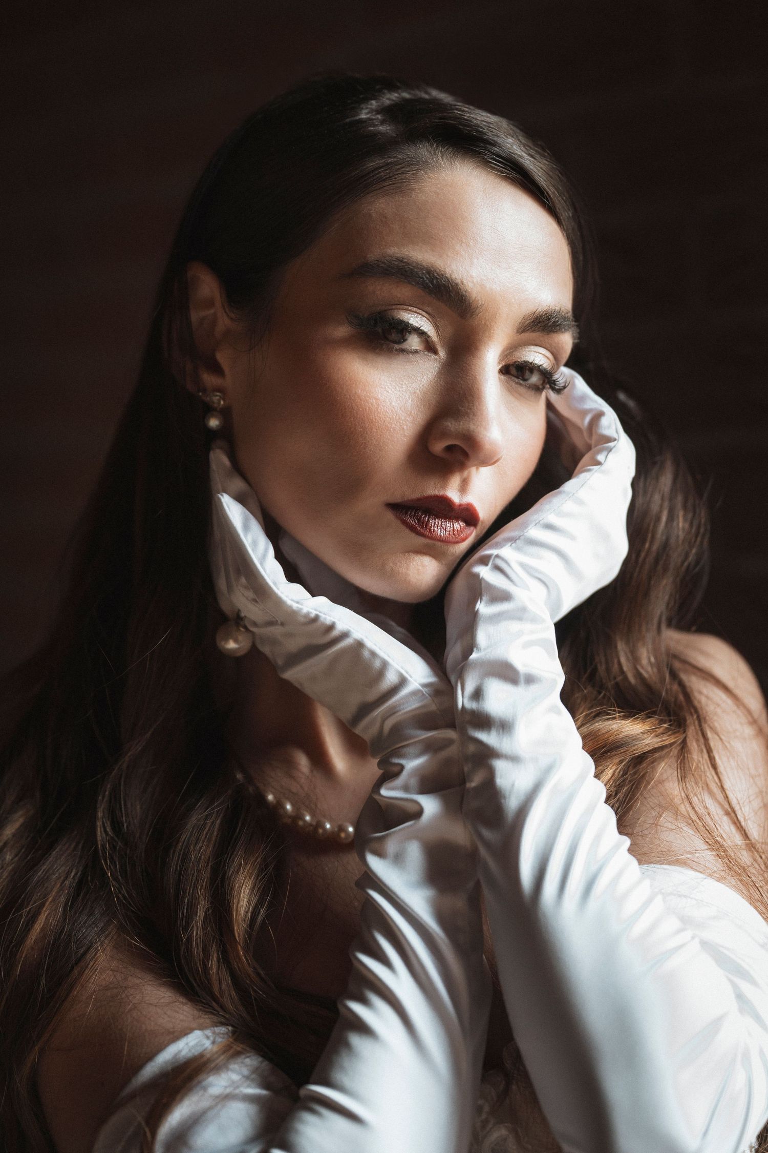 Figure in white gloves and pearl necklace poses dramatically against dark background.