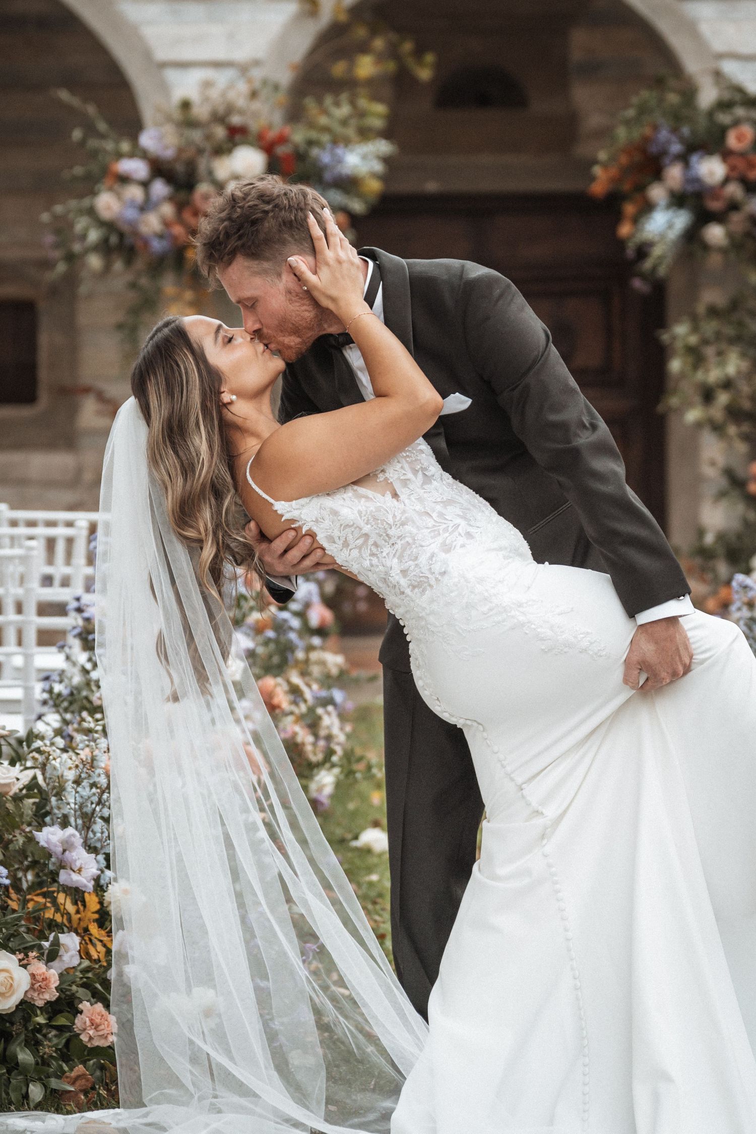 Romantic wedding dip kiss with flowing white dress and floral decorations.