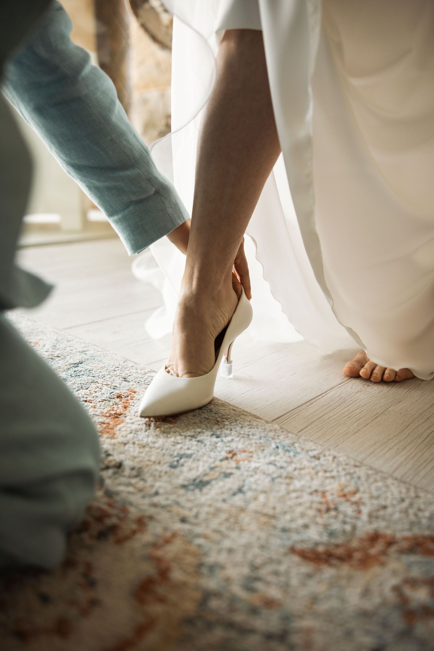Feet in white wedding dress and casual shoes standing on a patterned carpet.