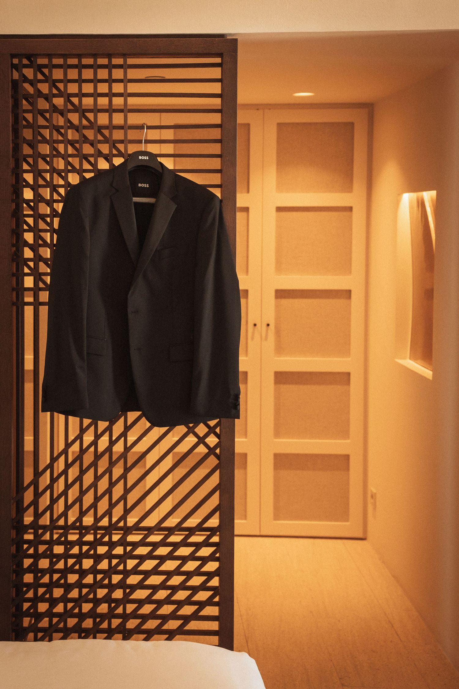 Dark suit jackets hanging on decorative lattice screens in warmly lit hotel hallway.