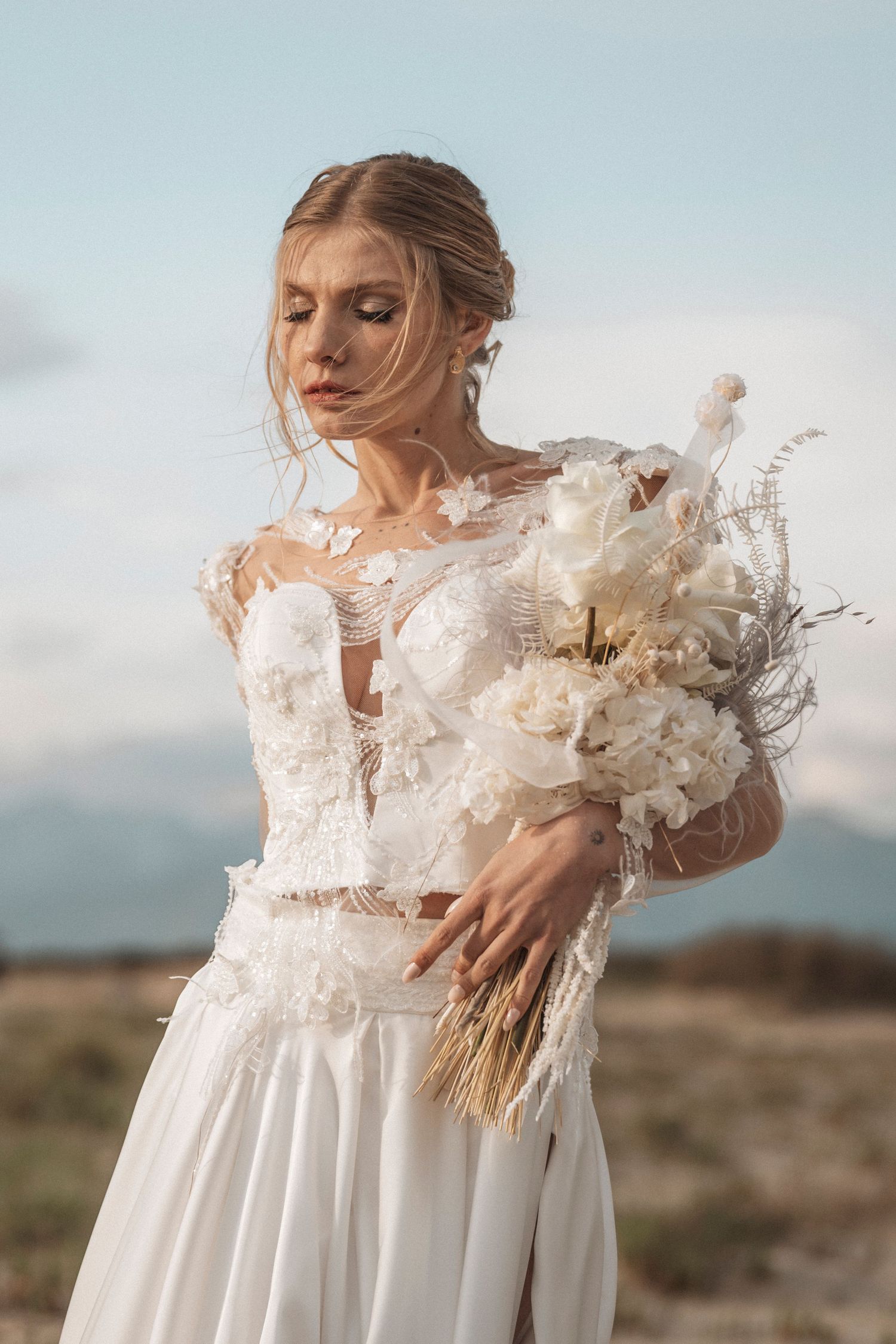 Romantic bridal portrait showcasing intricate feather details and flowing fabric in desert setting.
