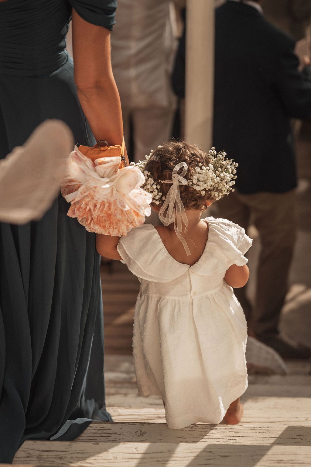 Little attendant in a white ruffled dress walking among formal-dressed guests at an event.
