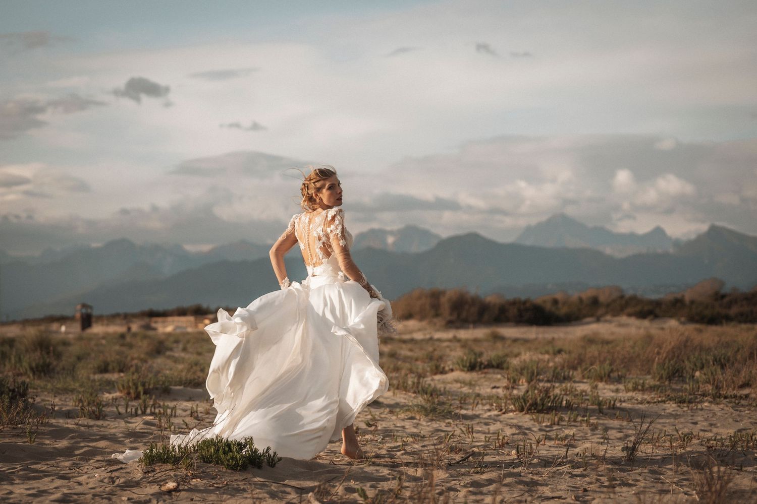 Panoramic desert wedding photography with mountains and flowing white dress in motion.