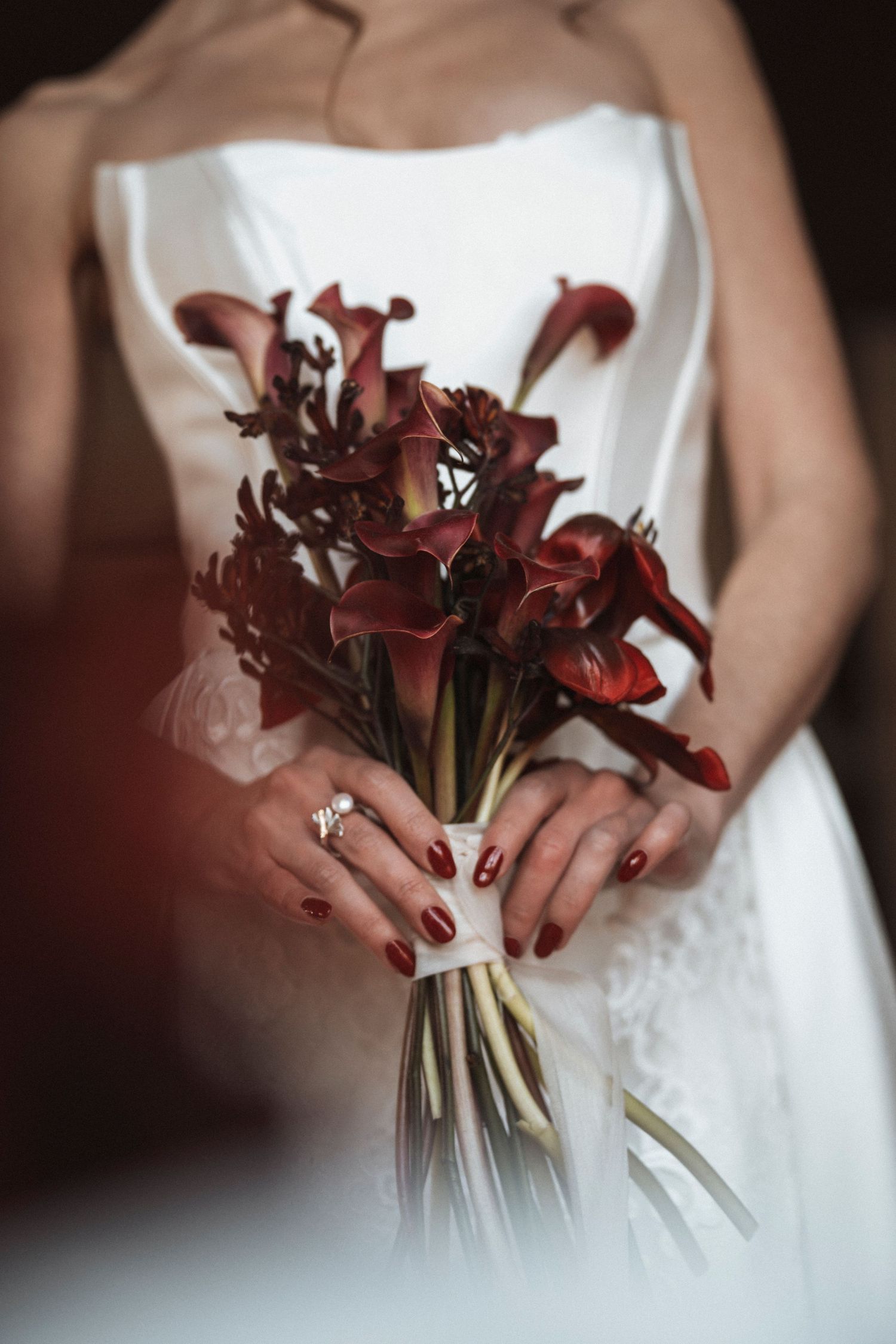 Deep red calla lily bouquet held against white wedding dress fabric.
