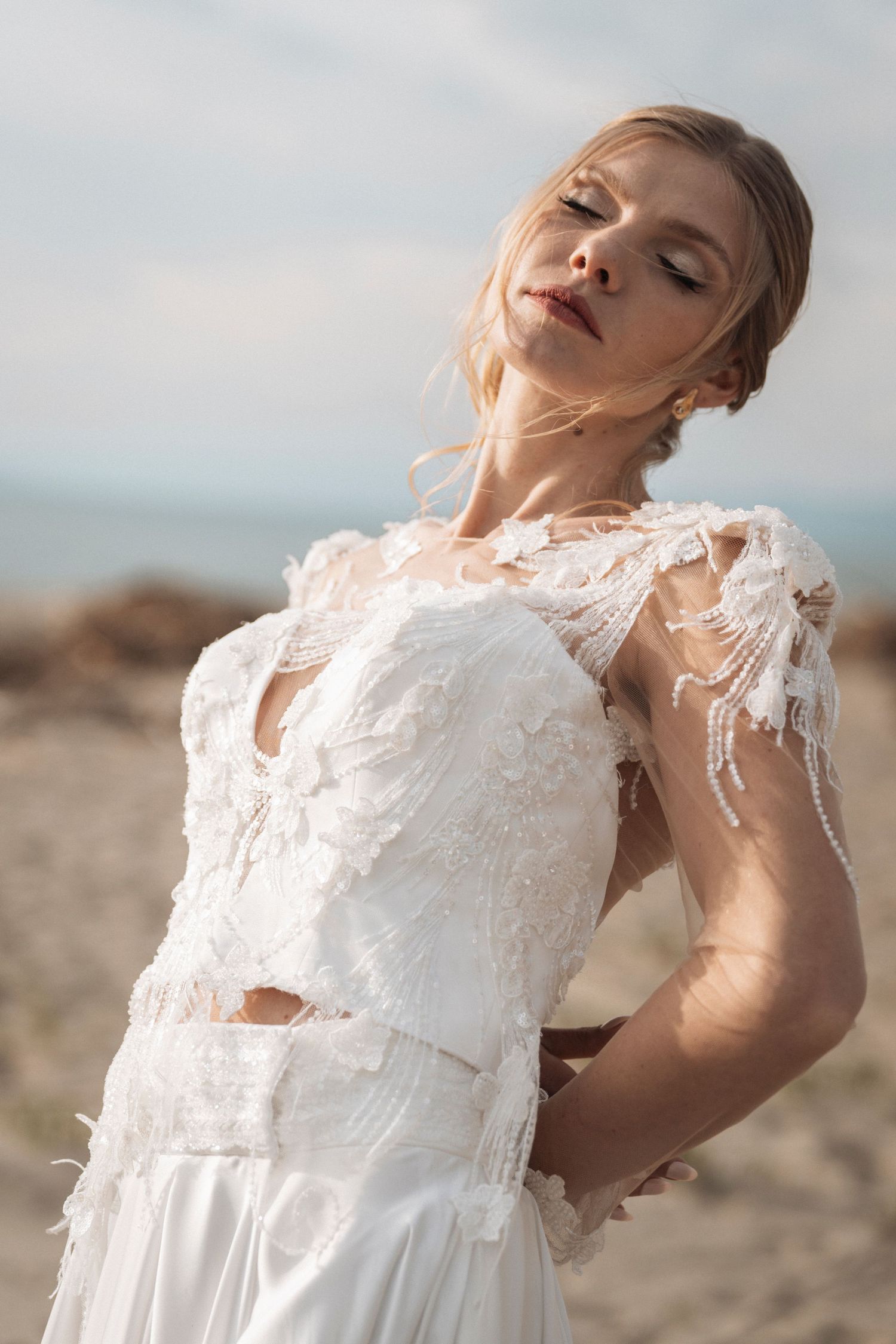 Ethereal bridal portrait featuring delicate lace details on a white wedding dress against a coastal backdrop.