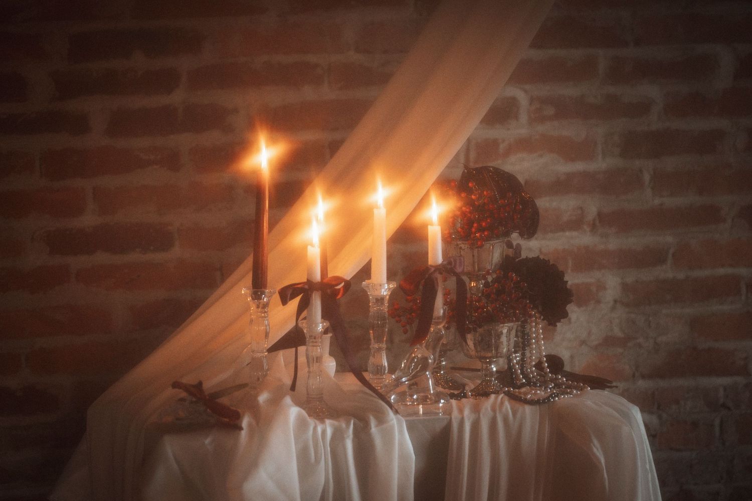 Three lit candles cast a warm glow against a rustic brick wall in a dark, moody setting.