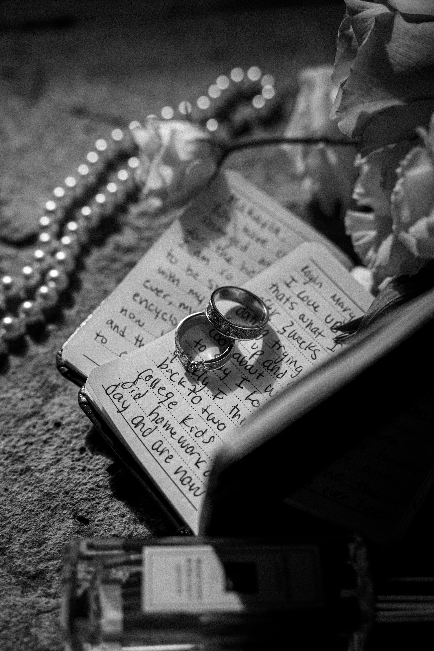 Wedding rings resting on handwritten note with pearl necklace.