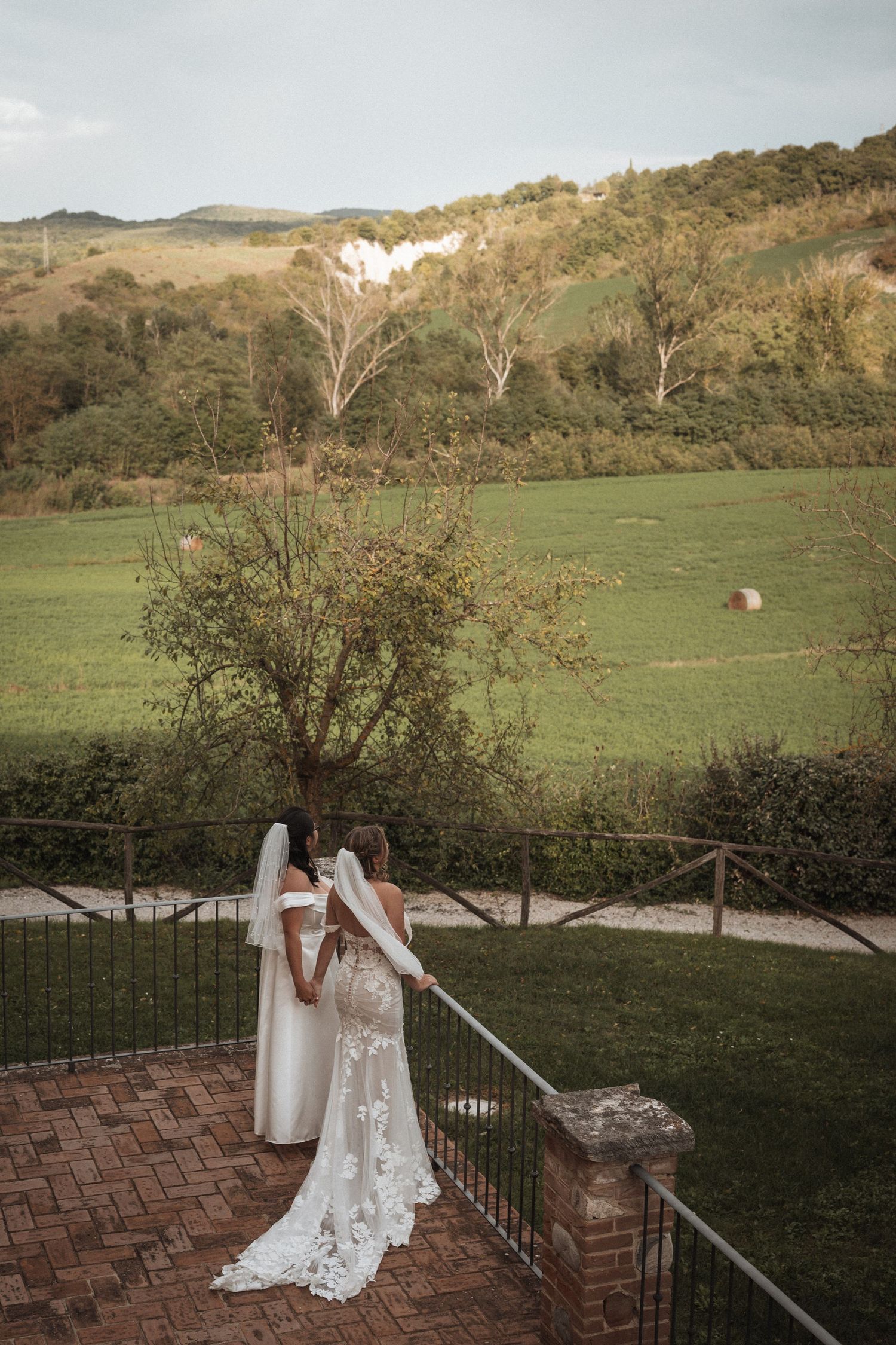A bride in a lace wedding dress poses on brick steps with mountain scenery in the background.