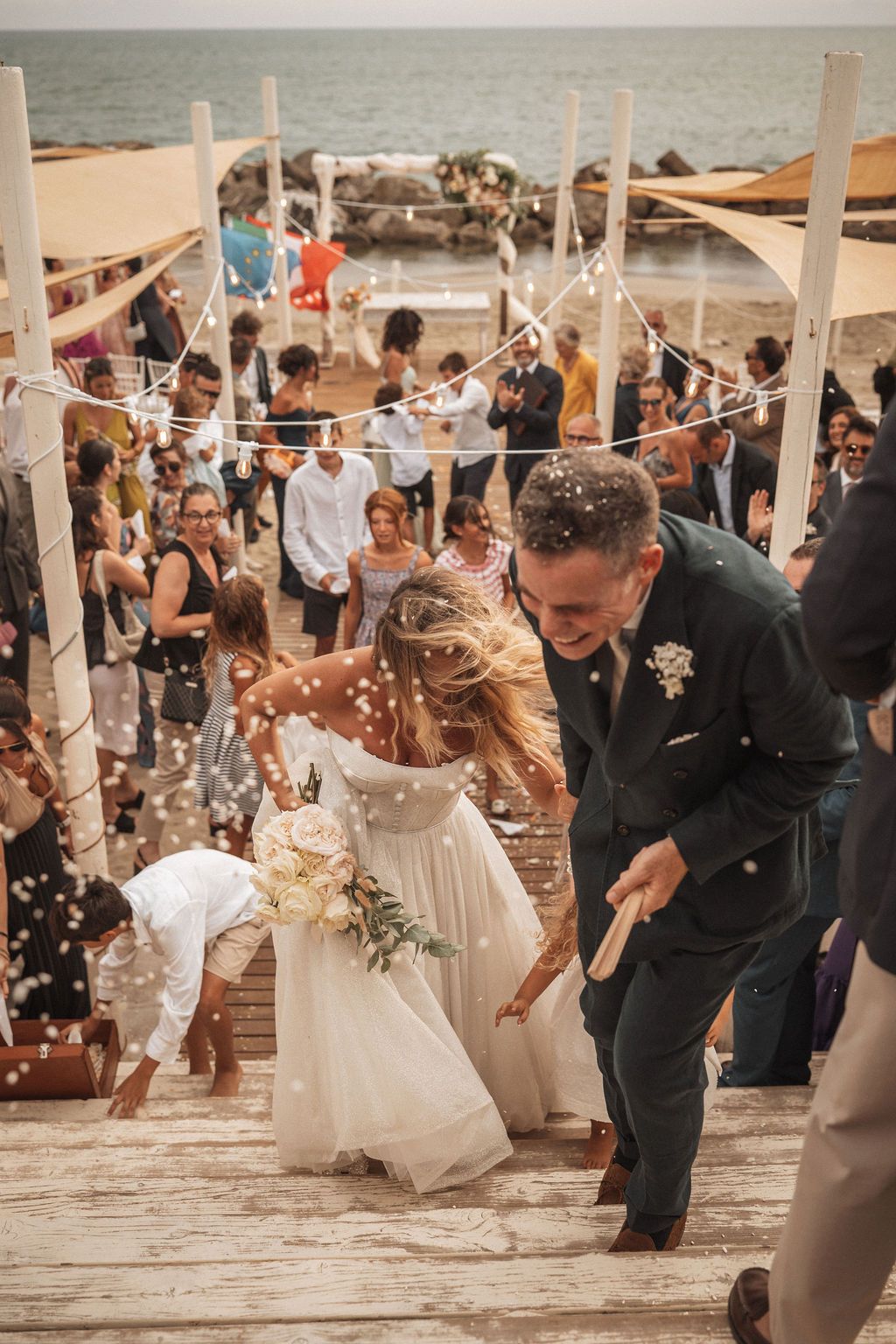 Wedding party celebrating with confetti on a seaside deck during golden hour.