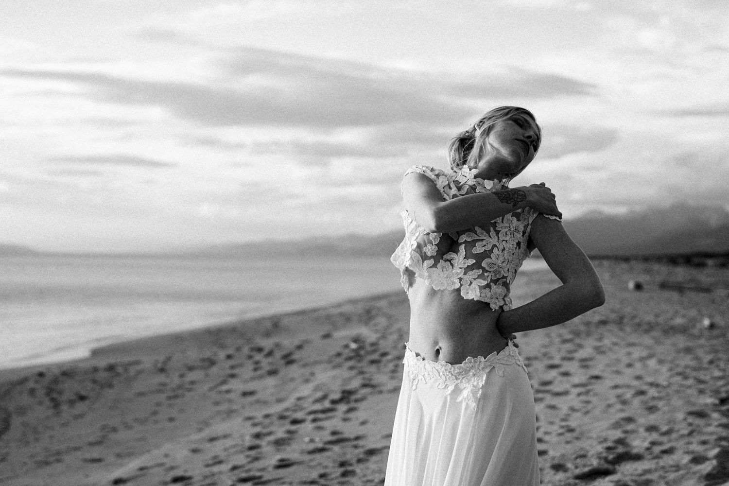 Black and white portrait of bride in two-piece wedding dress on sandy beach.