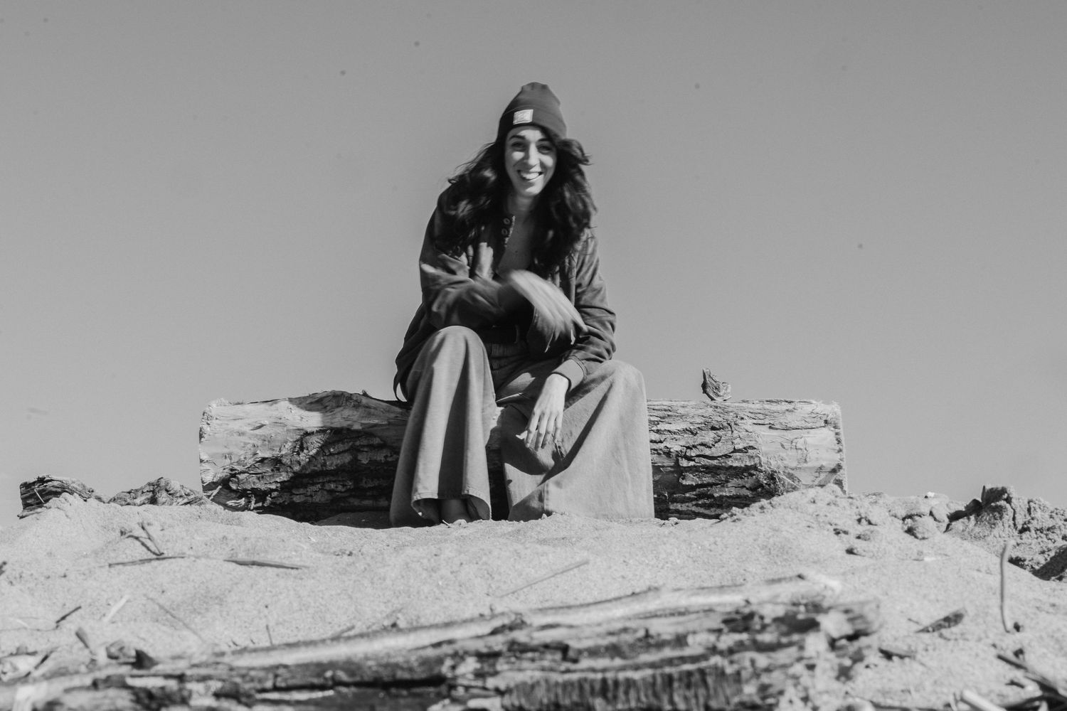 Vintage black and white portrait of someone sitting on logs in winter clothing.