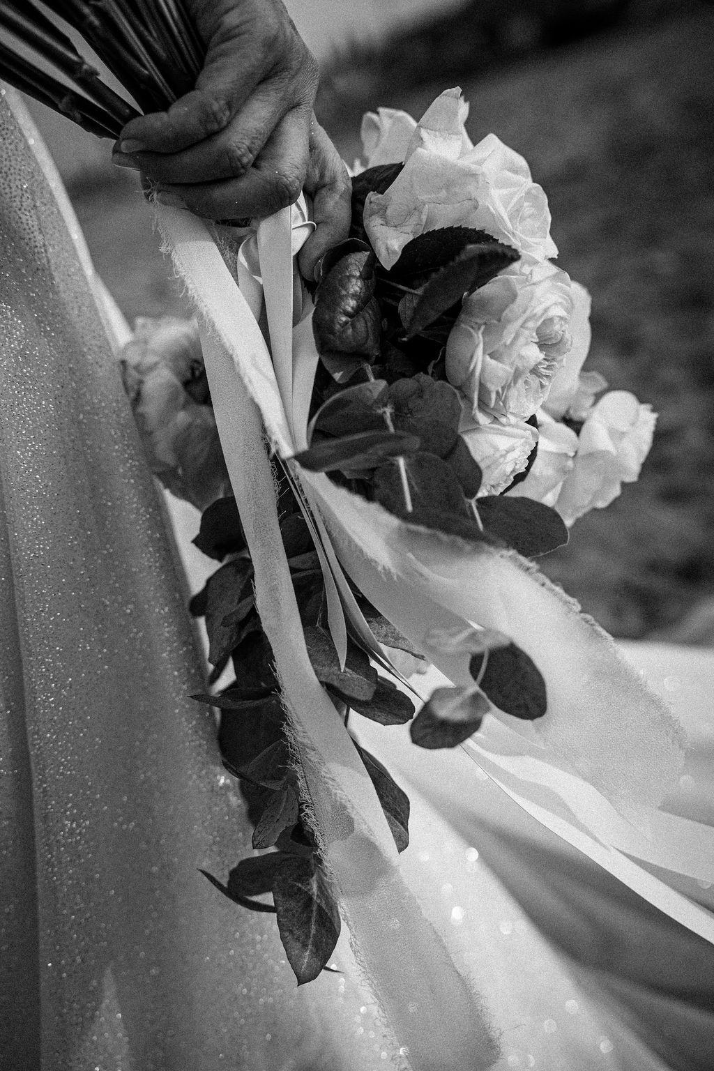 Black and white detail of white flowers and ribbons against a wedding dress.