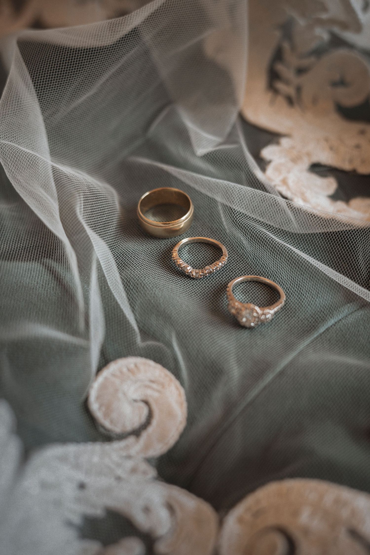 Wedding rings and delicate lace details arranged on soft tulle fabric in an artistic flatlay composition.