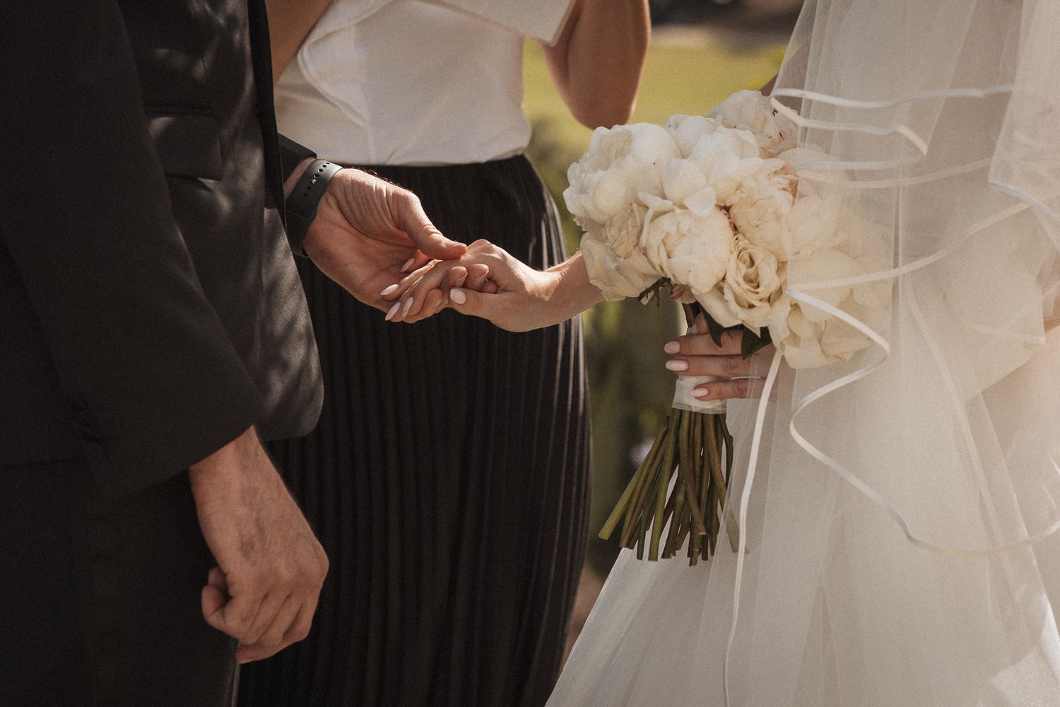 Elegant wedding party members in black and white attire pose together outdoors on a sunny day.