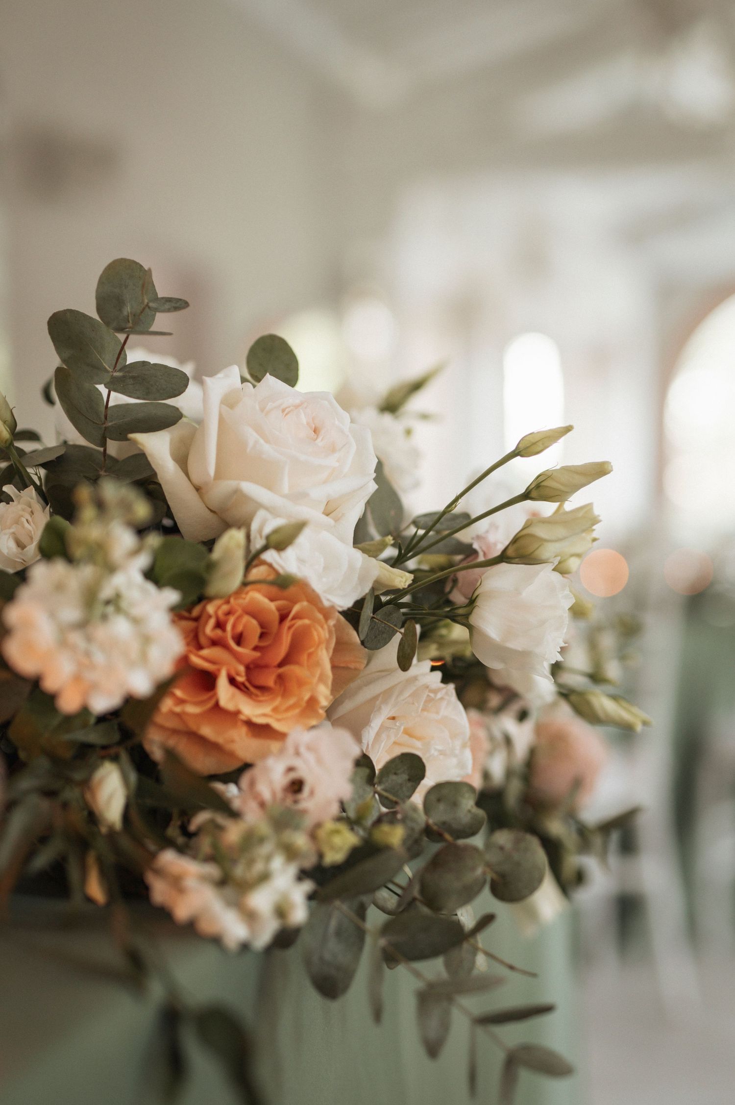 Elegant floral arrangement with peach roses and eucalyptus leaves in soft focus.