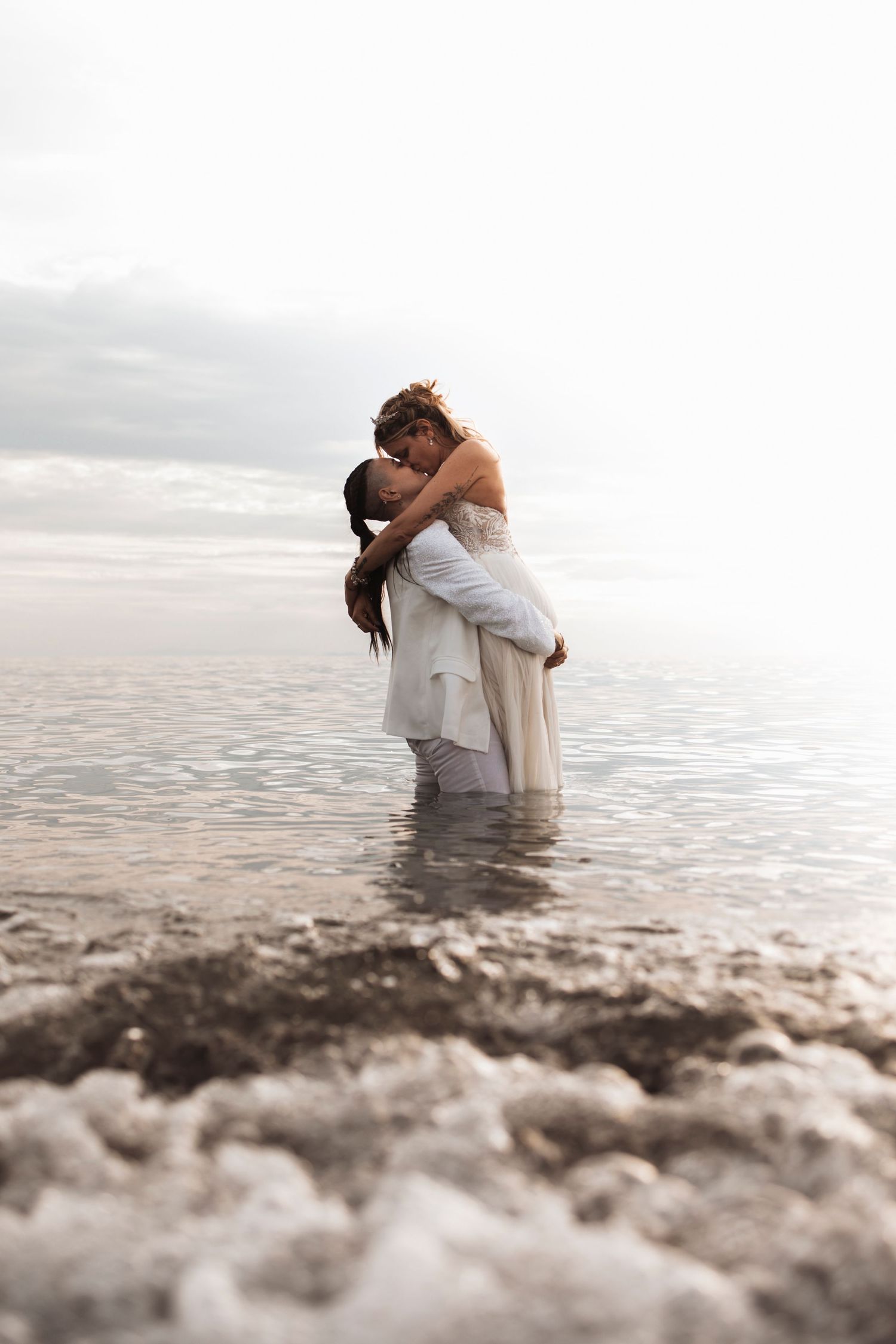 Romantic couple embracing in shallow ocean water during sunset.