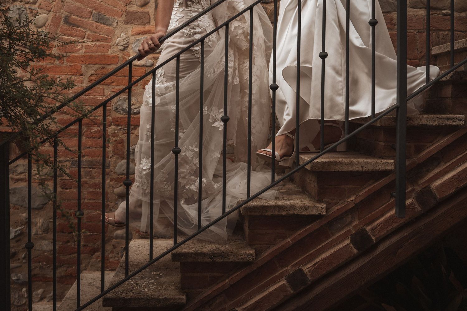 Detail shot of a wedding dress train flowing down rustic brick stairs with iron railing.