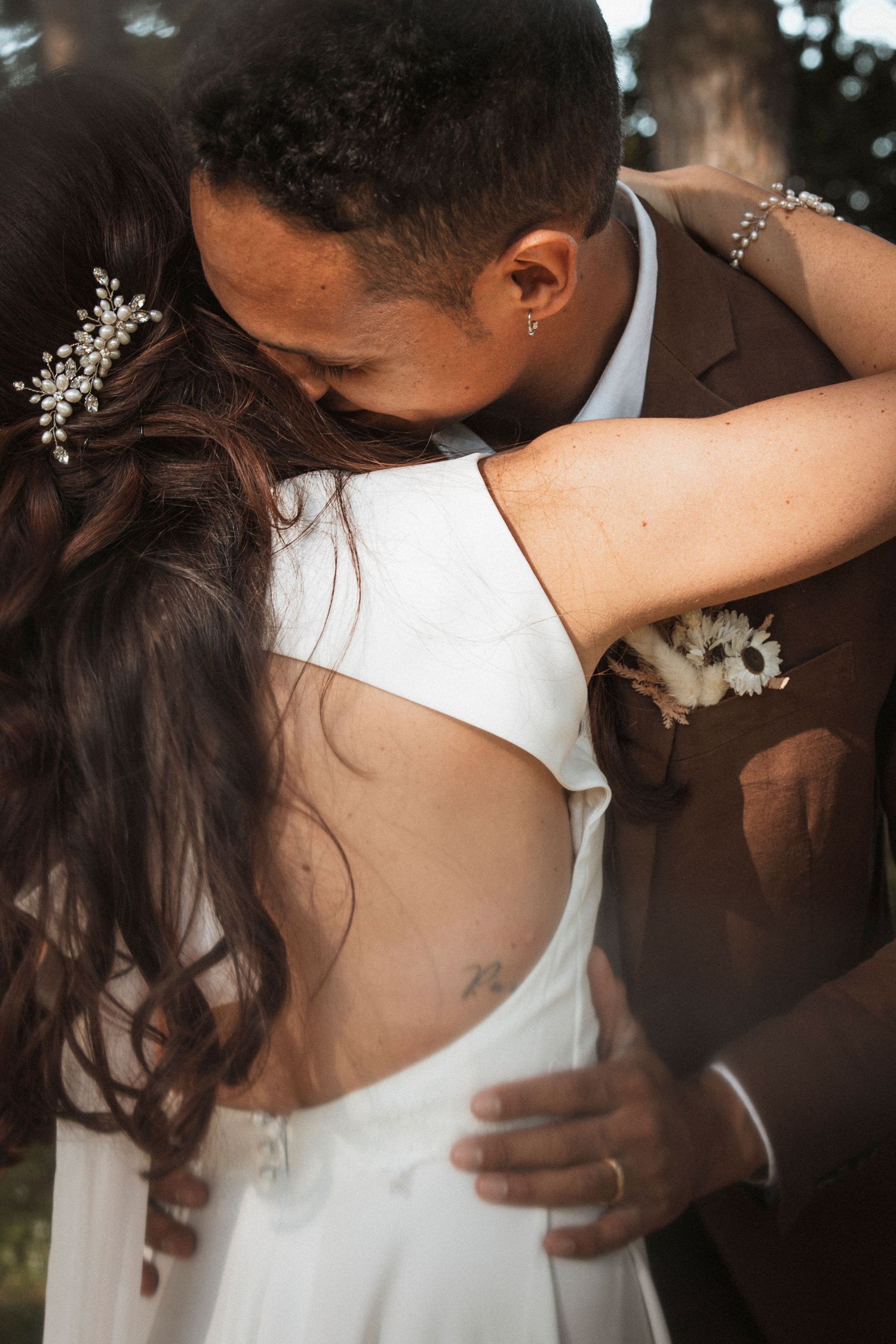 A romantic wedding couple embraces in an intimate dance pose wearing white and brown formal attire.