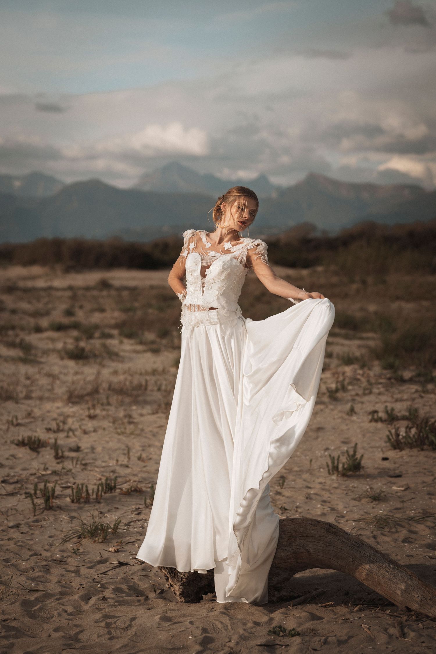 Flowing white wedding dress billows in the desert wind with dramatic mountain backdrop at sunset.