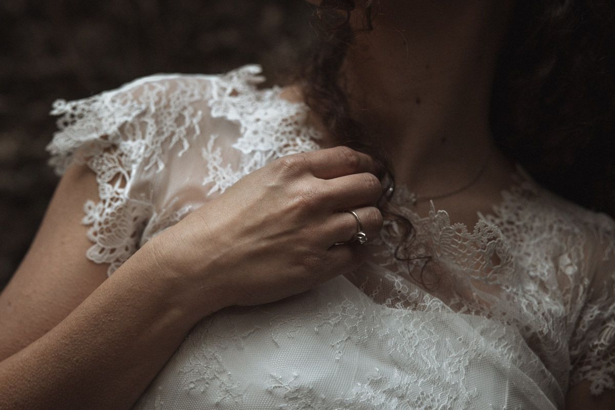 Close-up detail of delicate white lace on a wedding dress with a hand gently touching the fabric.