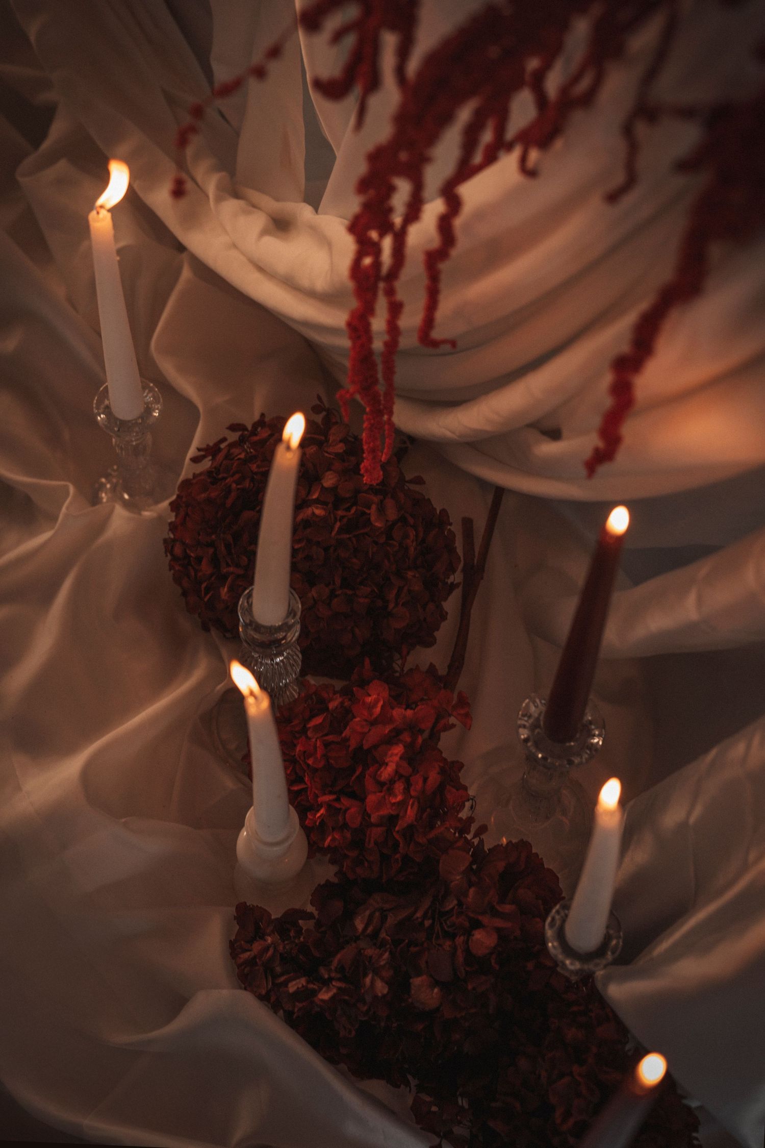 White candles and red flowers create a romantic holiday ambiance against a soft white background.