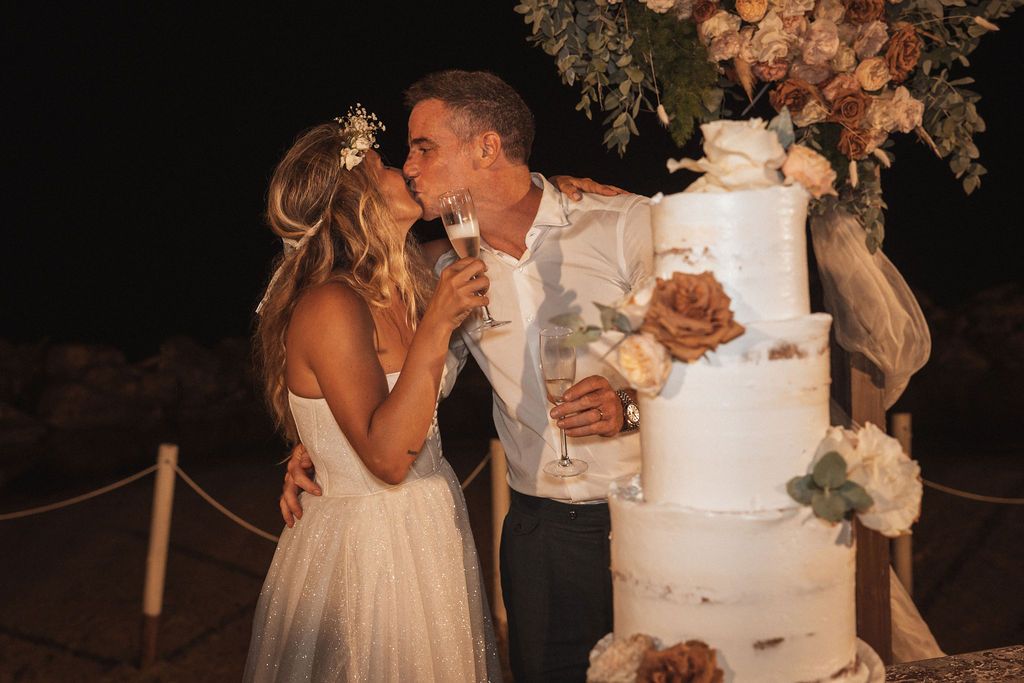 Wedding cake cutting ceremony under floral archway at night.