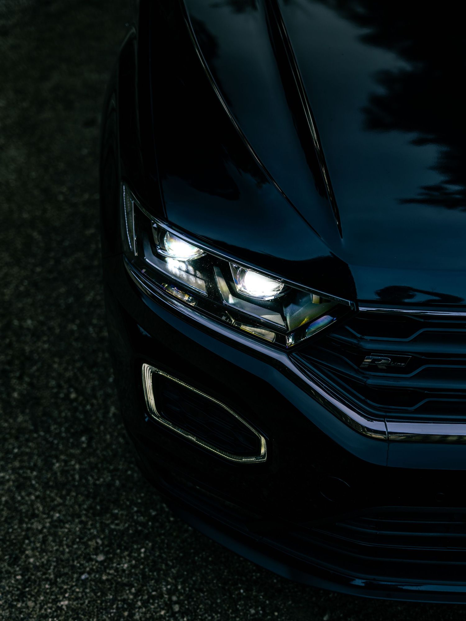 Close-up of a sleek black Volkswagen T-Roc LED headlight and front grille detail.