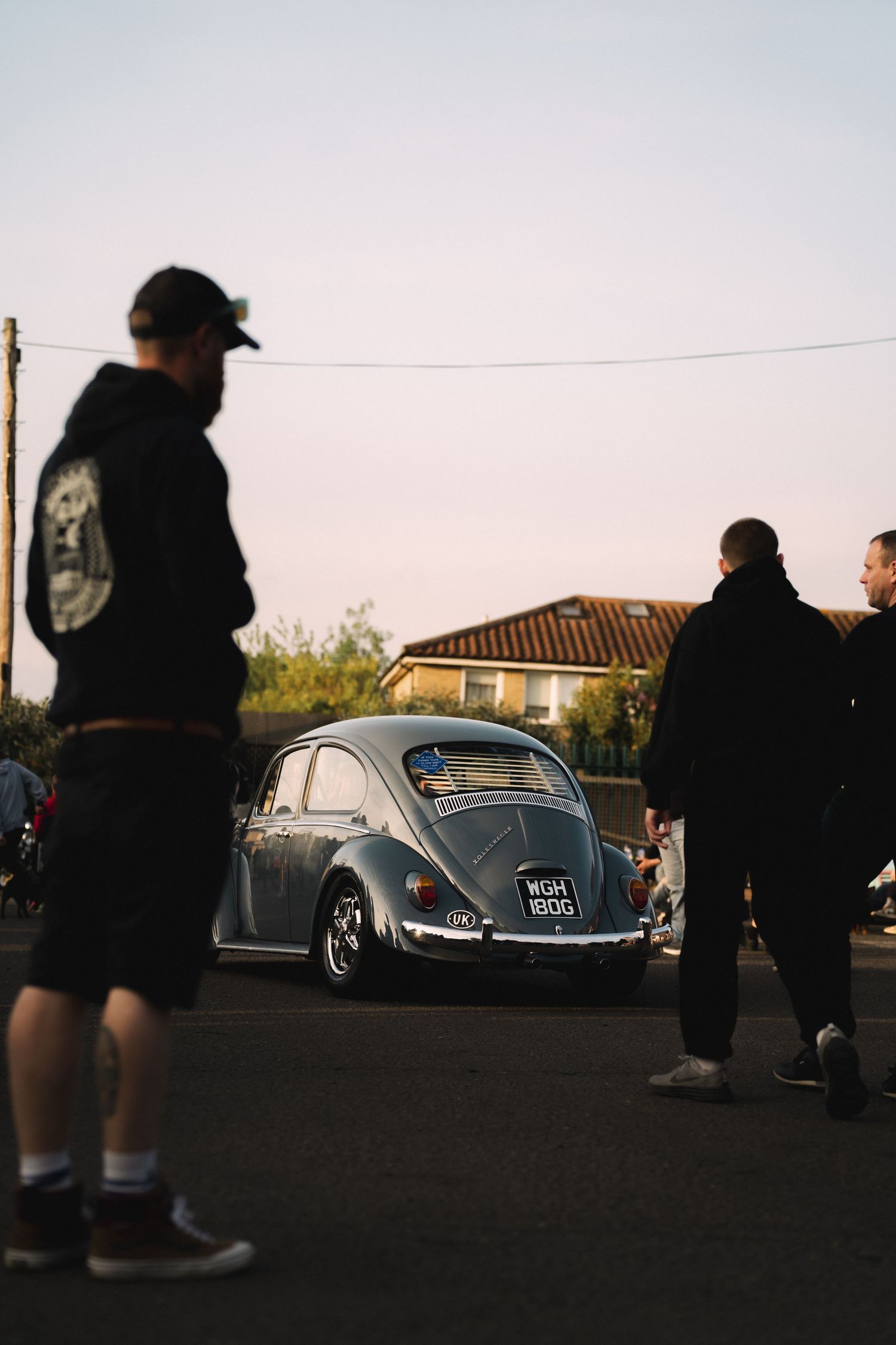 A lowered VW Beetle surrounded by people at a car meet during golden hour.